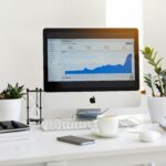 Home A clean, contemporary workspace featuring a desktop with analytics on the screen and plants for a fresh look.